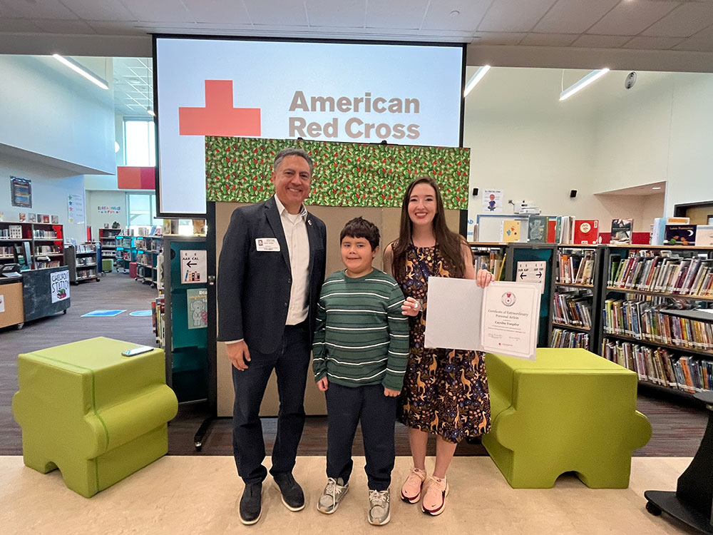Javier Valdez standing next to a Elementary School child and teacher in a school library.
