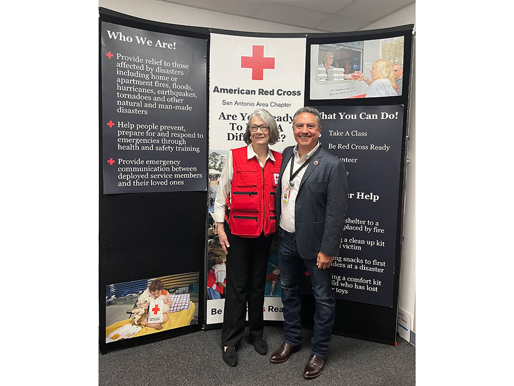 Javier Valdez and Kate Forbes stand next to a large Red Cross informational sign.