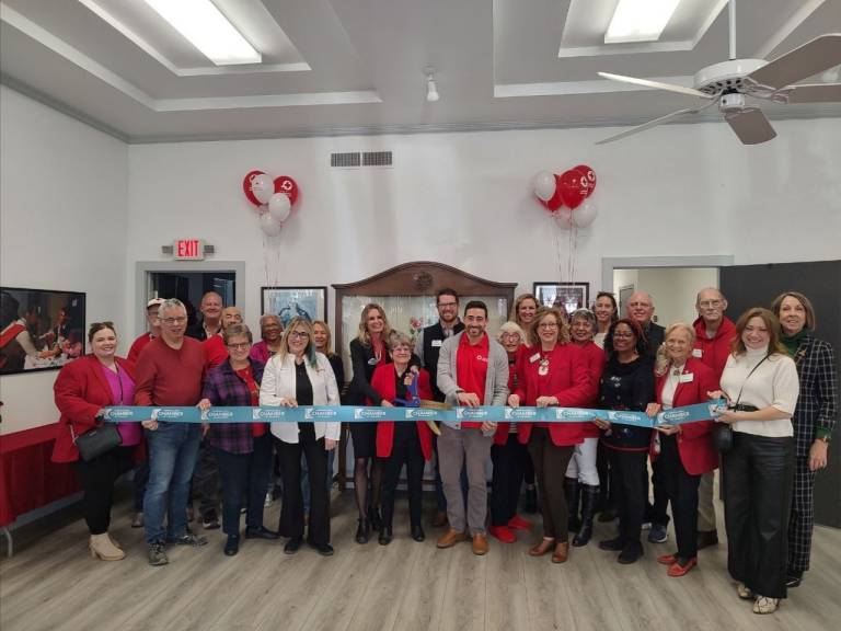 A group of people standing behind a horizontal ribbon, at a ribbon cutting ceremony