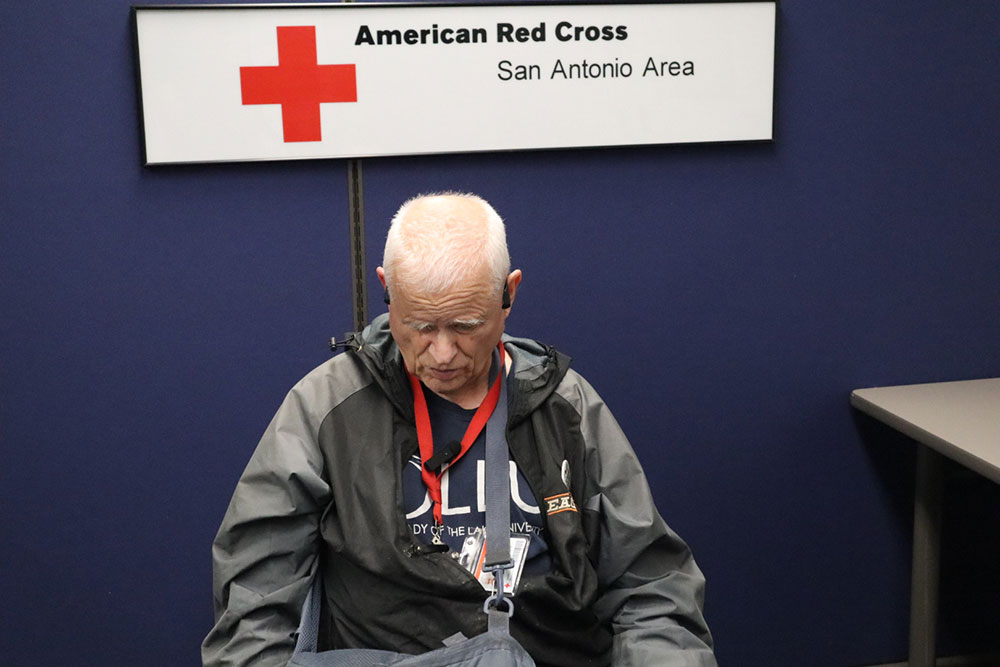 Red Cross volunteer Larry Roser sitting down qith a Red Cross San Antonio Area sign behind him.