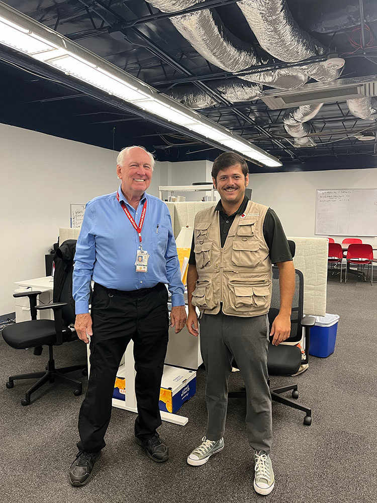 Nick Richardson wearing a Red Cross vest while standing and smile with a Red Cross staff member.