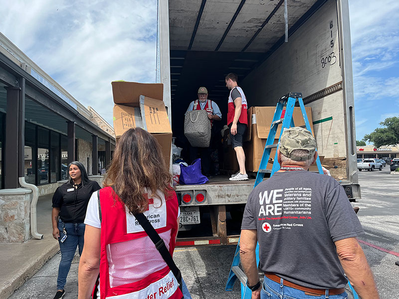 Red Cross volunteers unloading a semi-truck that's parked next to a building.