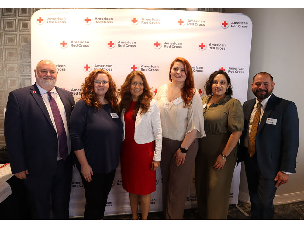 A group of women and men standing together in front of a Red Cross banner and smiling.
