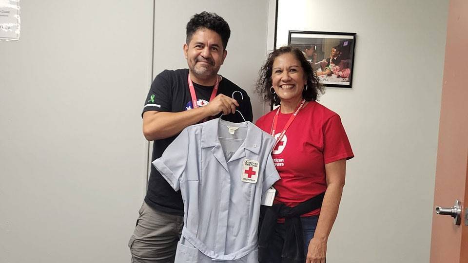 David Saucedo and another red cross volunteer posing with a vintage red cross nurse's dress.
