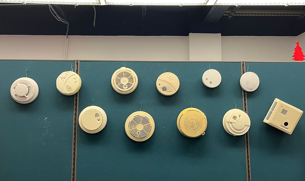 collection of old smoke alarms hanging on an office cubicle wall.