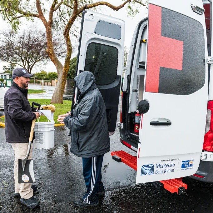 2 Red Cross volunteers in back of truck with supplies.