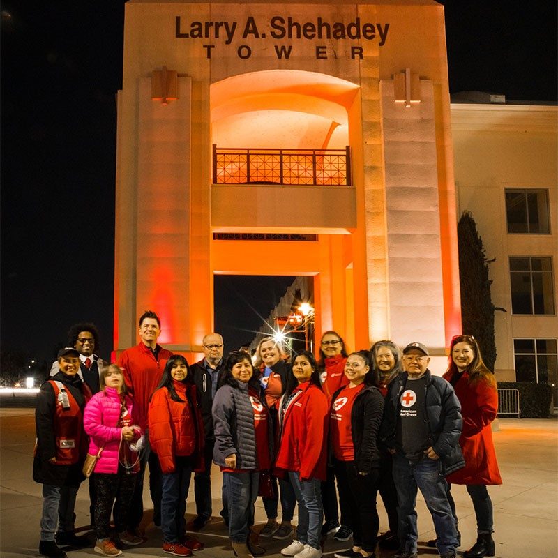 Red Cross volunteers group shot in front of lit up building.