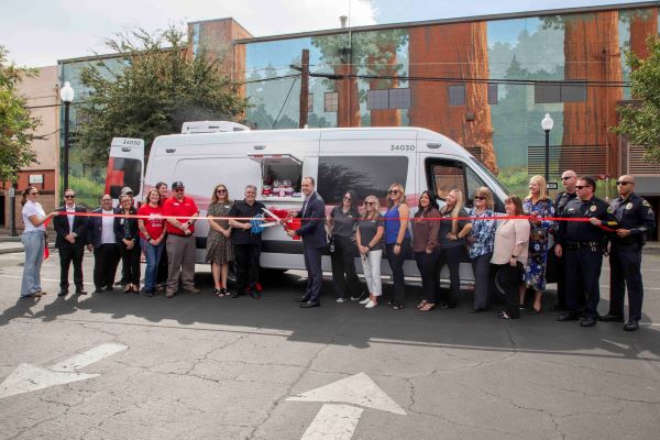A group of people standing in front of a white van for a ribbon cutting