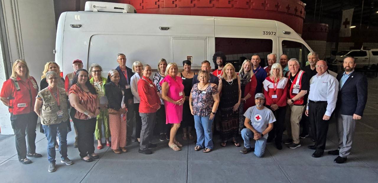 a group of people both sitting and standing posing in front of a Red Cross emergency vehicle