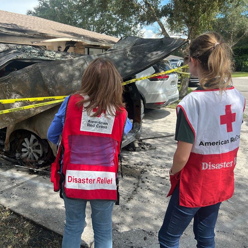 2 Red Cross volunteers looking at burnt car and garage.
