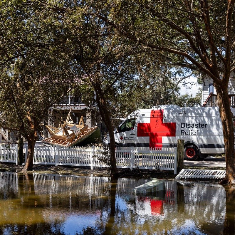 Red Cross Disaster Relief van by lake and trees and damaged building.