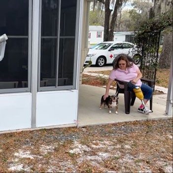 Lady in chair on porch petting small dog.