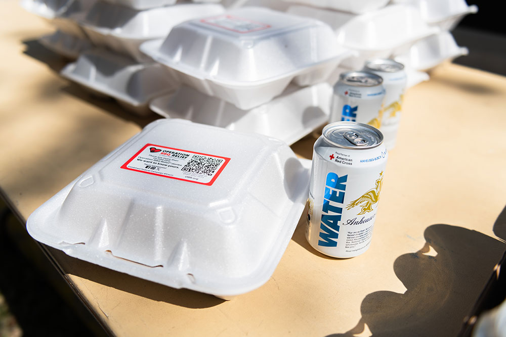 Food in to go containers and canned water sitting on a table.
