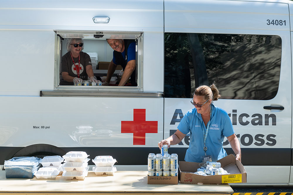American Red Cross volunteers serve packed food and water from an American Red Cross vehicle.