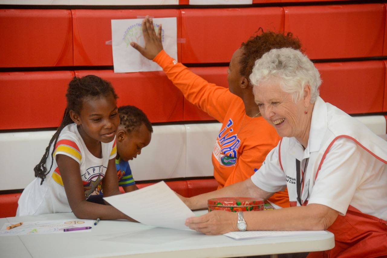 September 2, 2019. Orlando, Florida.
American Red Cross volunteer Lindsay Stroh teaches and sings a song about hurricanes with 7-year-old Tessiyah at the Red Cross evacuation center at Edgewater High School. The song is an original composition by Lindsay, is sung to the tune Good Night Irene, and teaches how hurricanes form, the difference between hurricanes and typhoons, and what to bring to a shelter when a hurricane is coming. Tessiyah is a resident at the shelter along with her mother Tasharay and 2-year-old sister Antoine.
Photo by Daniel Cima/American Red Cross