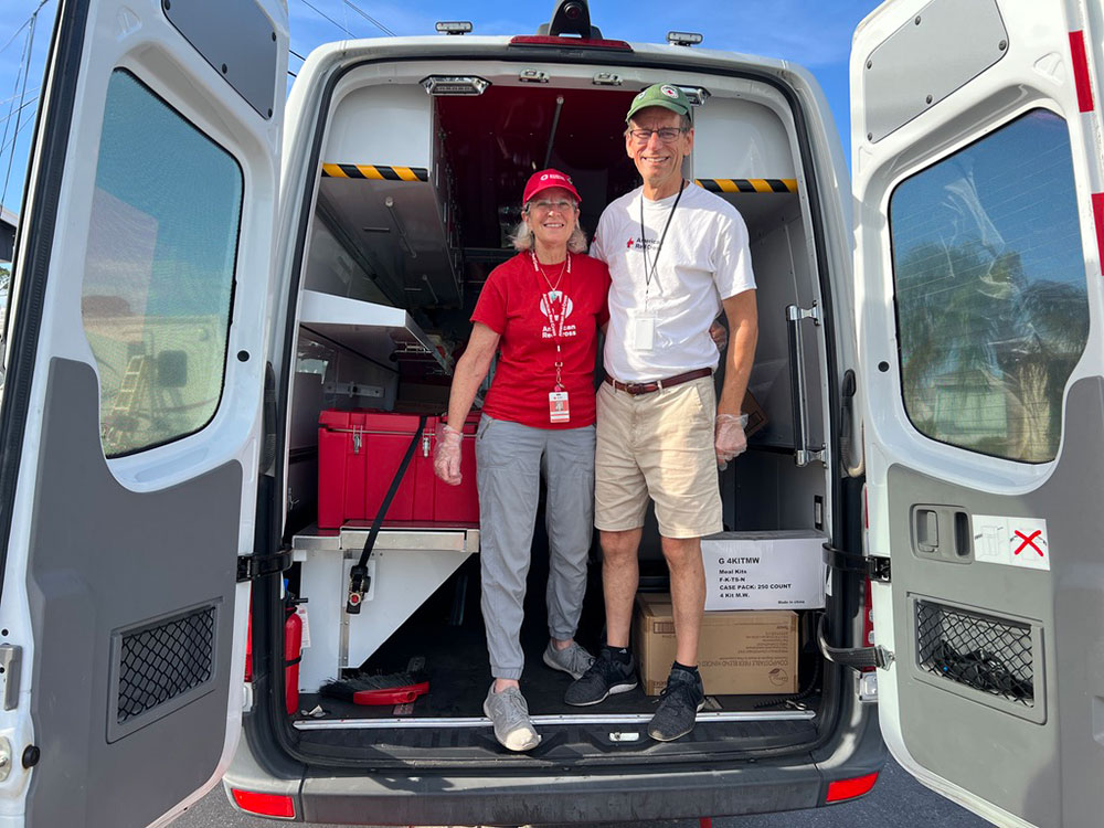 Jeanne and Doug Reinelt standing in back of Red Cross Emergency Response Vehicle with it's back doors open. 