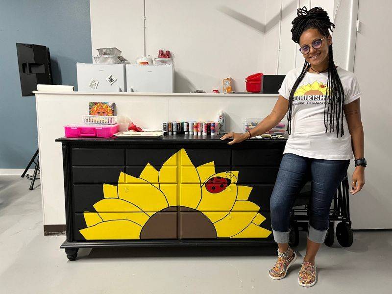 margie pierrelouis standing in front of flower painted desk