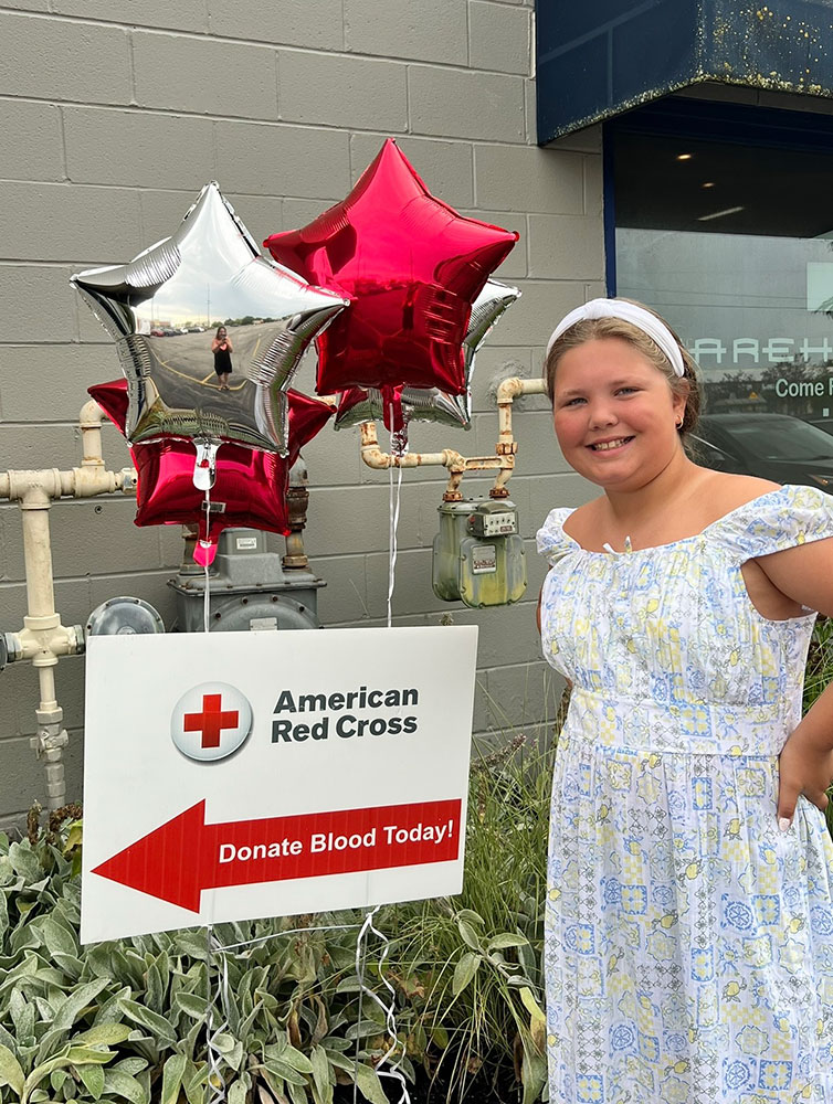 Allie Harris smiling while standing next to a Red Cross blood donation sign and balloons.