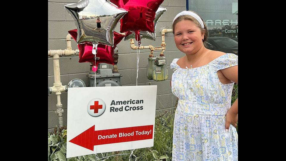 Allie Harris smiling while standing next to a Red Cross blood donation sign and balloons.