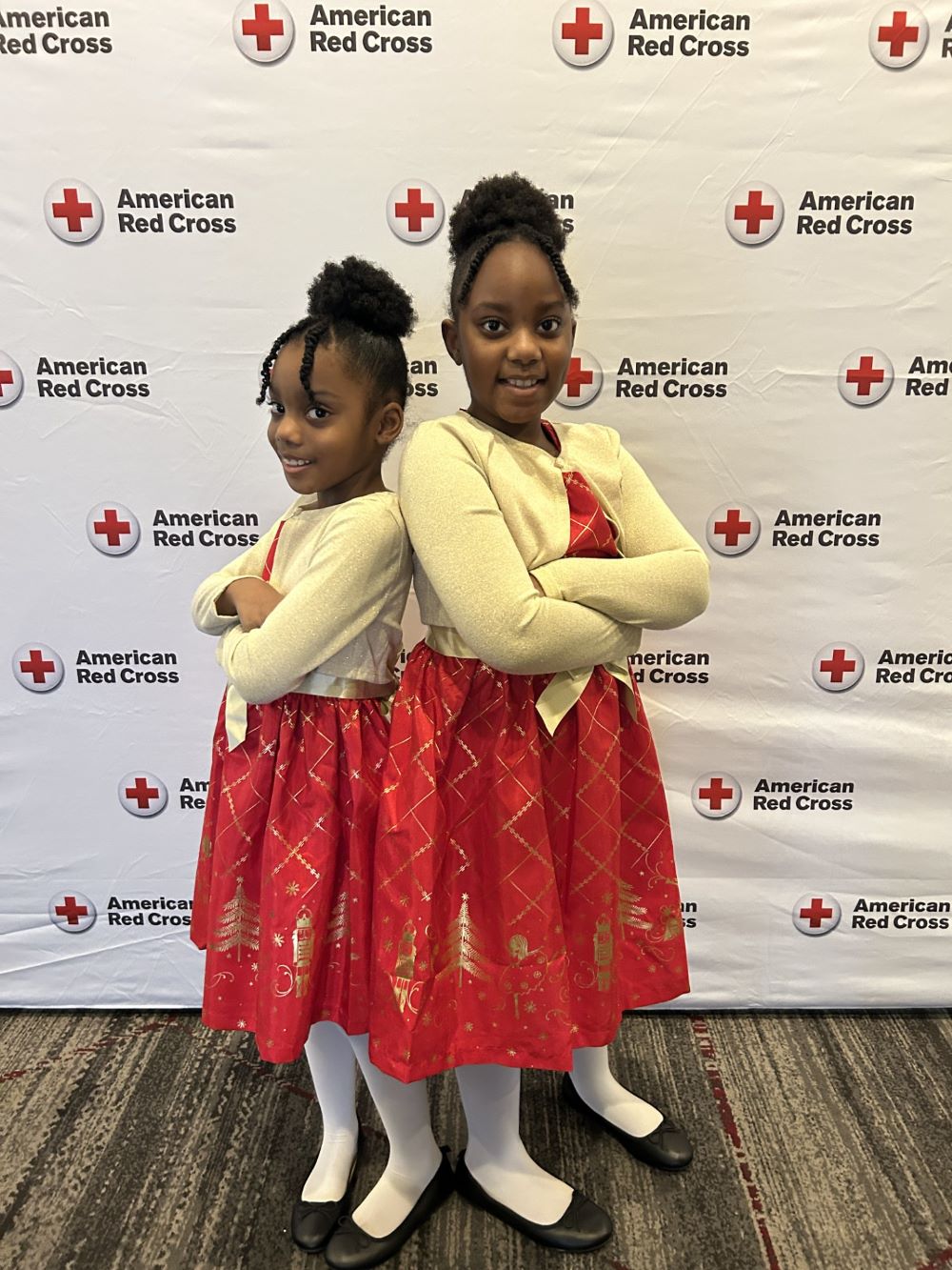 Cicelia and Brianna Dobson smiling next to a red cross banner