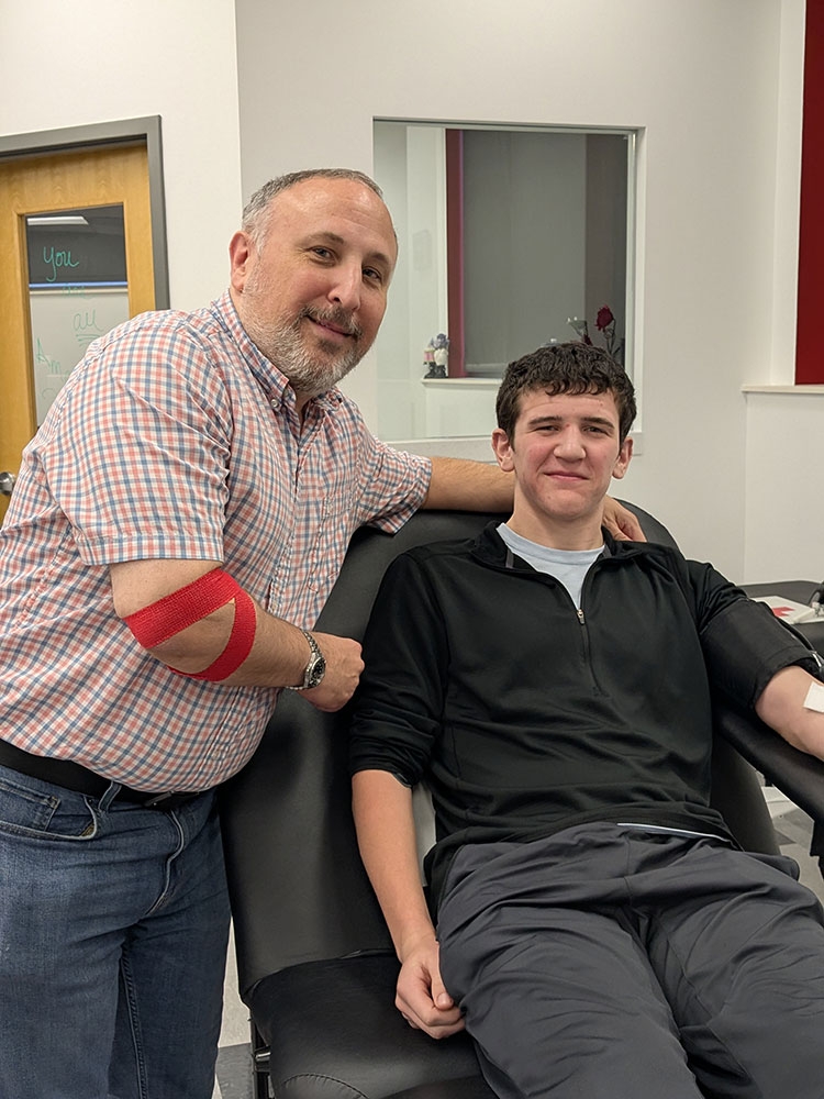 Chuck Saletta with his arm around his son, who is sitting in a chair, after donating blood.