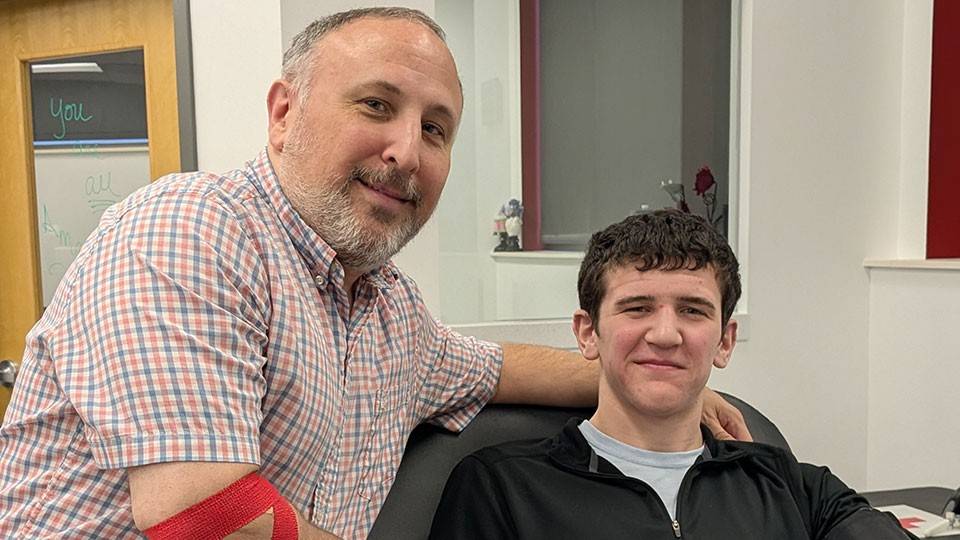 Chuck Saletta with his arm around his son, who is sitting in a chair, after donating blood.