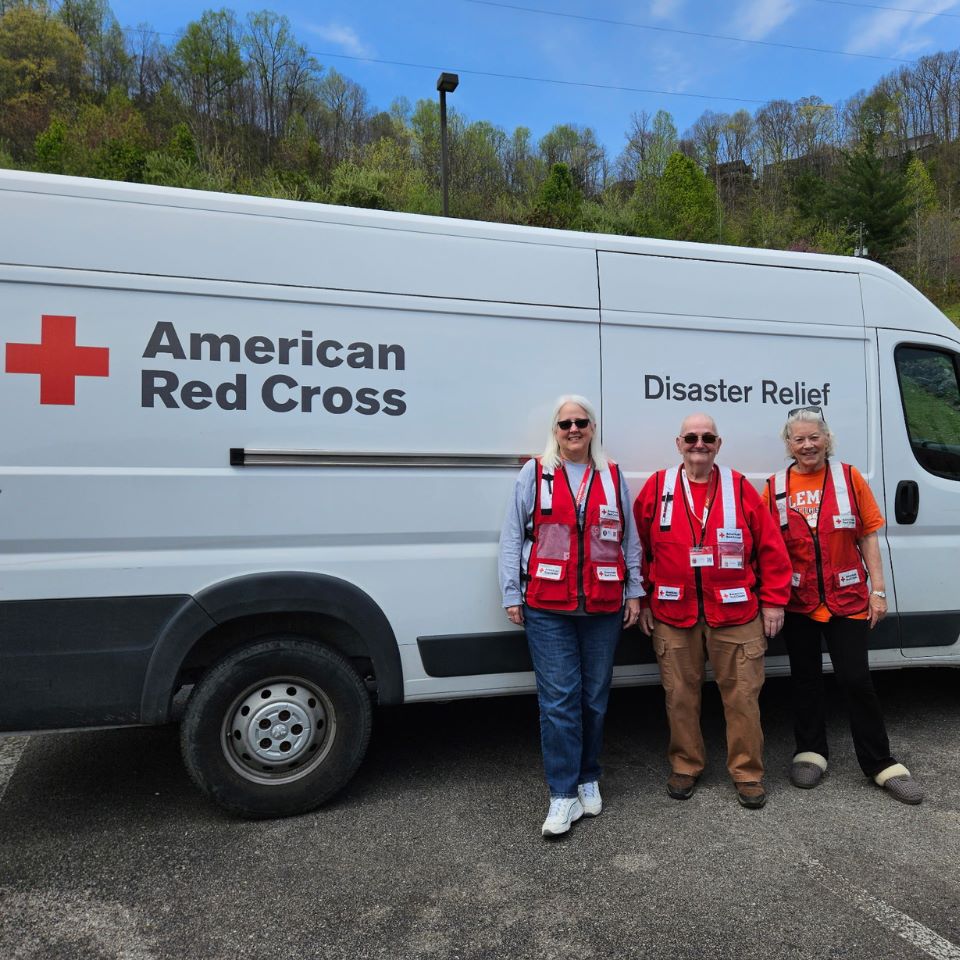 Debbie standing next to two Red Cross volunteers in front of an emergency response vehicle