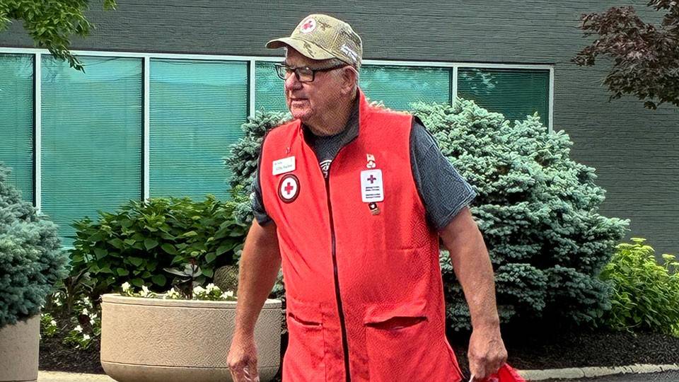 Jeff Earley wearing a Red Cross vest and holding a Red Cross bag while walking on the pavement.