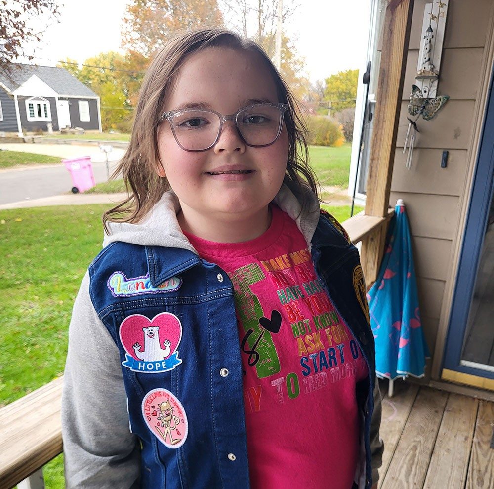 London Hamilton standing on a porch, wearing glasses and a denim jacket.
