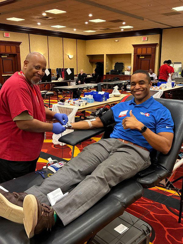 a Red Cross nurse drawing blood from a donor who is sitting in a chair smiling and giving a thumbs up.