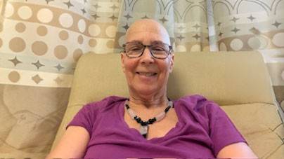 Norma Wasserstrom sitting in chair wearing glasses a necklace and smiling.