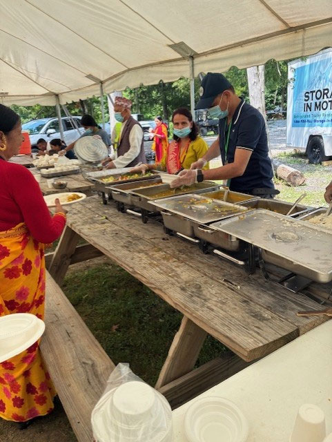 people catering food with chafing dishes on picknick tables under a canopy.
