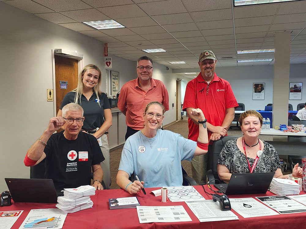 three people sitting at a table with promotional items and three people standing behind them in an office.