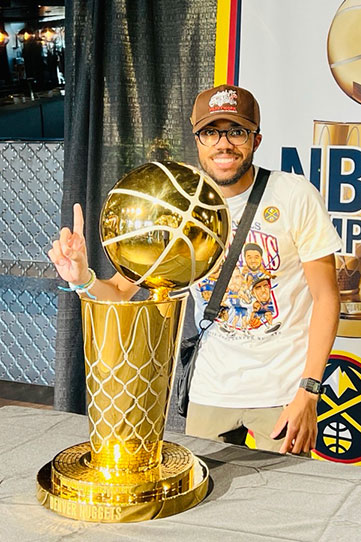 Jordan Davis wearing hat and glasses and giving the number one sign next to a NBA championship trophy.
