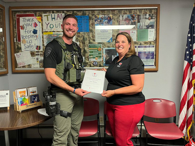 A police officer and Red Cross volunteer holding an award during a presentation.