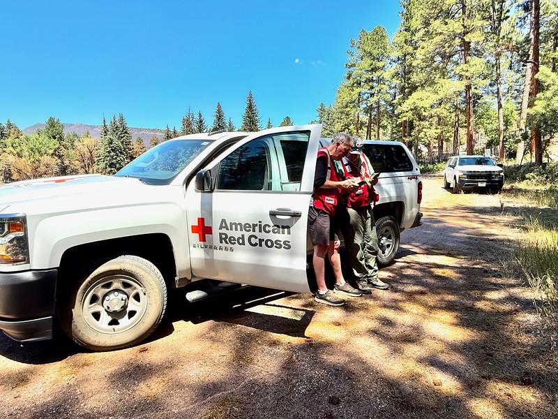 Red Cross volunteers stand outside next to a Red Cross vehicle