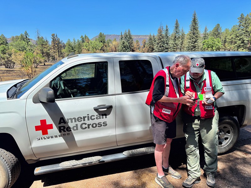 Red Cross volunteers stand outside next to a Red Cross vehicle