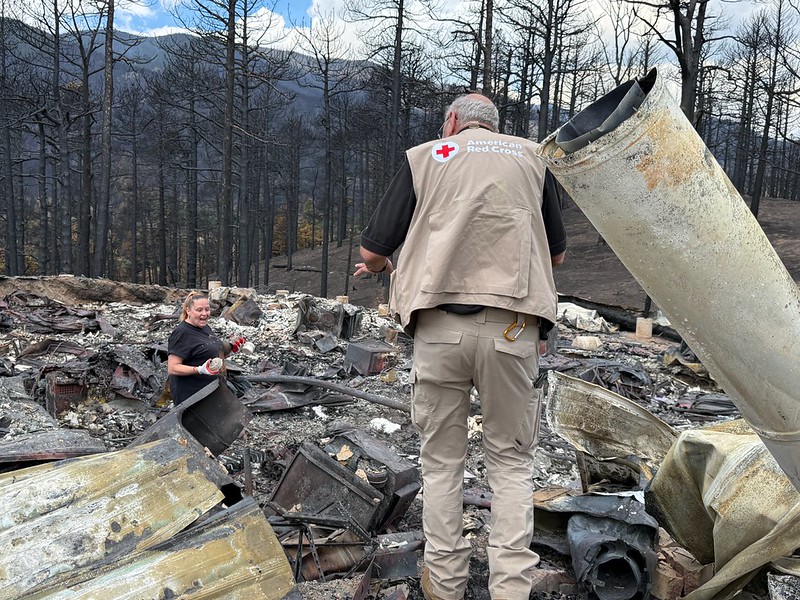 A woman sorts through the burnt remains of a home while a Red Cross volunteer talks with them from atop a pile of rubble.