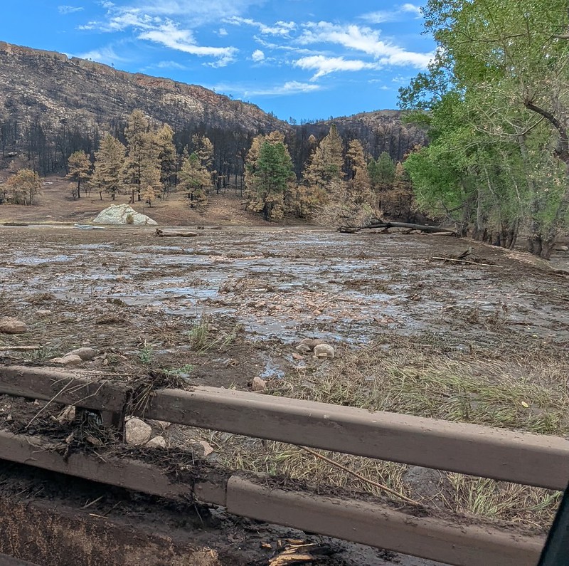 Water moves downhill, with a bridge in the foreground and debris in the water flow