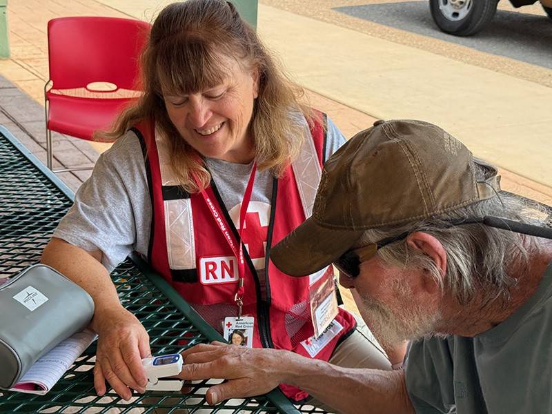 A woman volunteering with the Red Cross takes a man's pulse and blood pressure