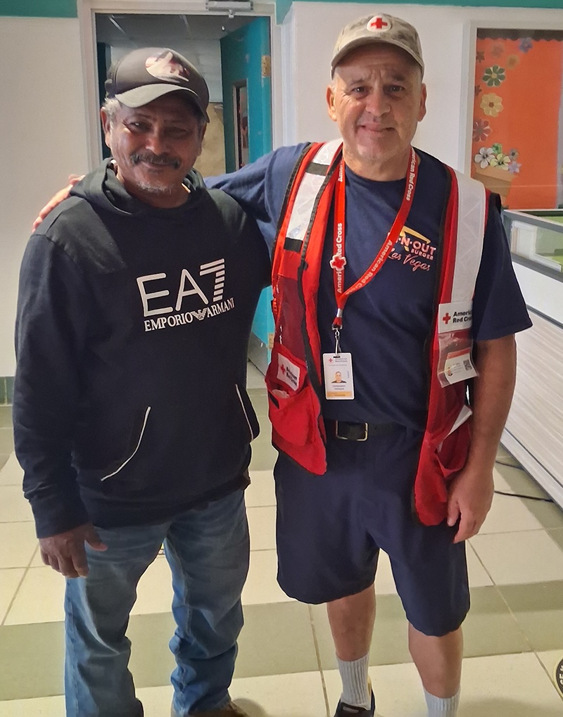 Two men, one in Red Cross gear, stand in a hallway together