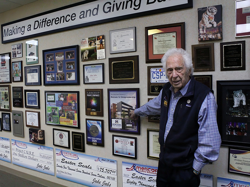 A man stands in front of a wall of various awards and plaques