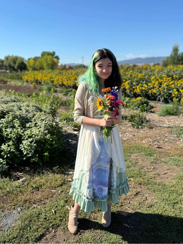 A smiling young girl stands in a garden, holding a bouquet of flowers in her hands.