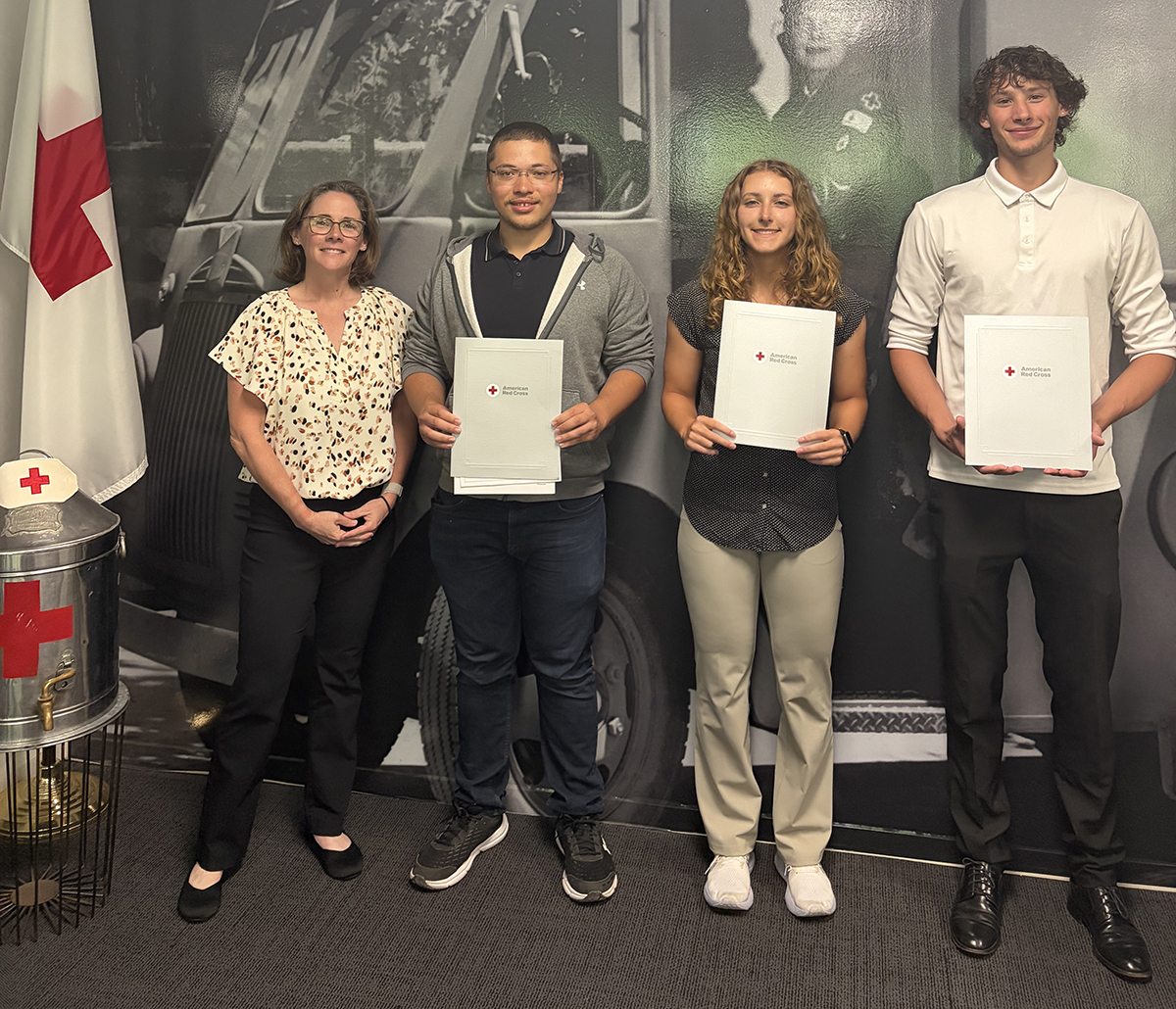 Four people standing together in front of a mural, with three holding lifesaving awards in their hands
