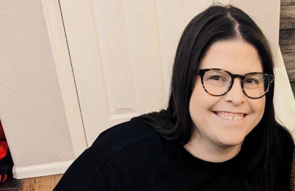 A woman dressed in black sits on the floor, smiling