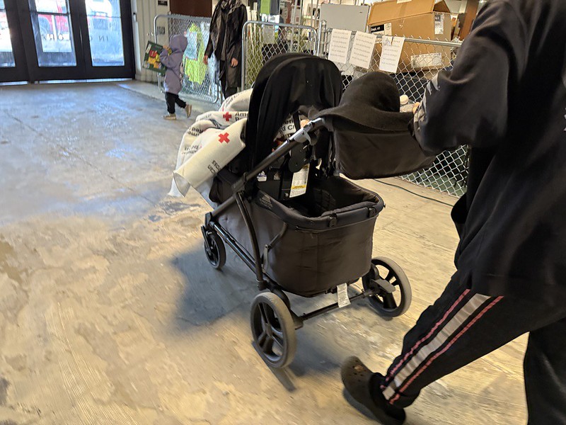 Man pushing a stroller with a Red Cross blanket visible