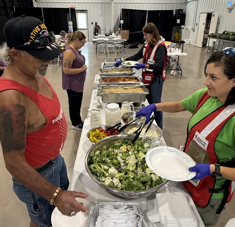 A Red Cross volunteer serves salad to a man in a shelter