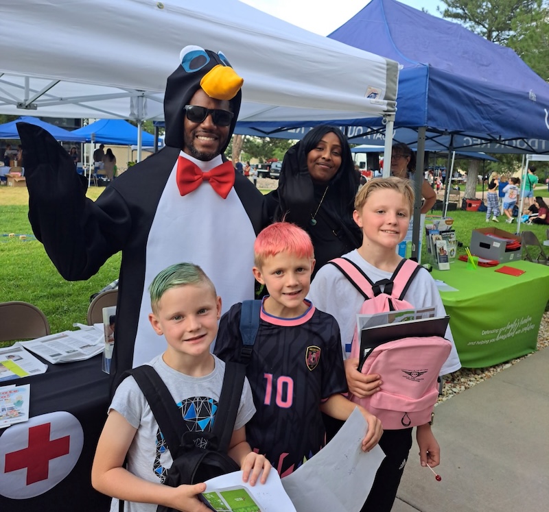 Pedro the Penguin stands with three young students