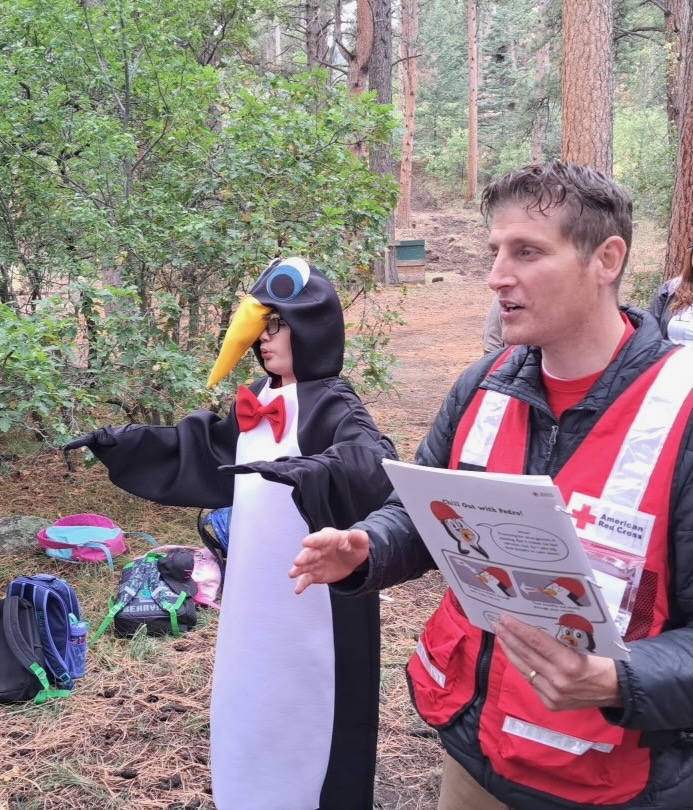 A Red Cross volunteer gives a lesson while a student dressed as Pedro stands next to him.
