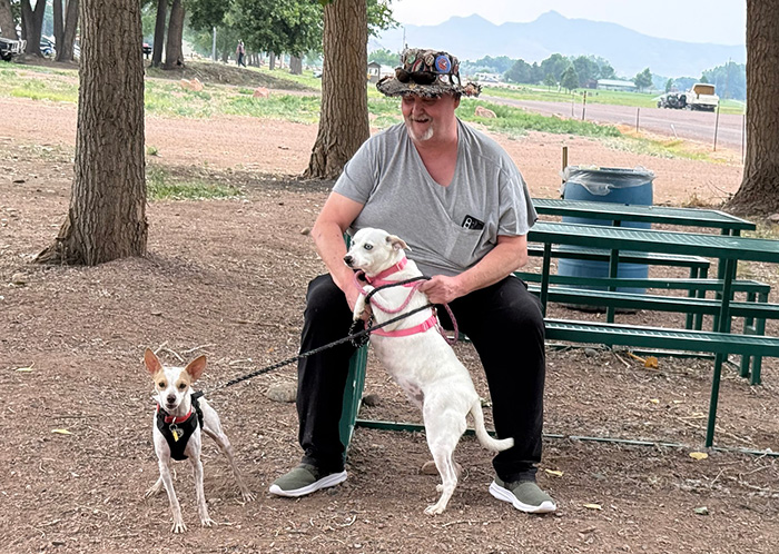 A man sitting outside on a bench with two dogs